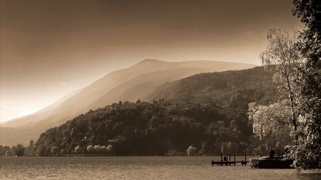 A tranquil mountain lake landscape enveloped in mist and sepia tones, creating a peaceful atmosphere.